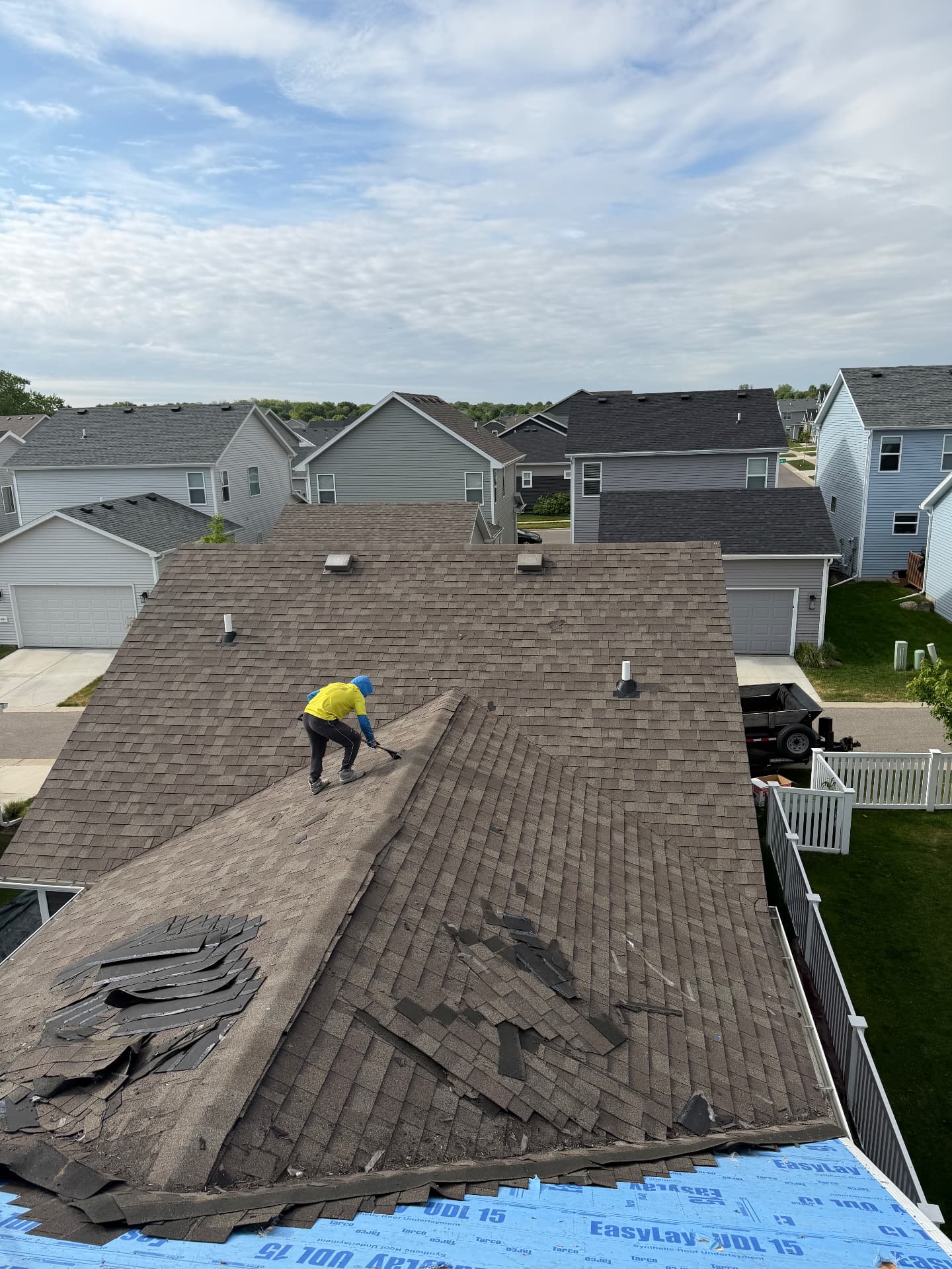 Roofer stripping storm-damaged shingles from a home